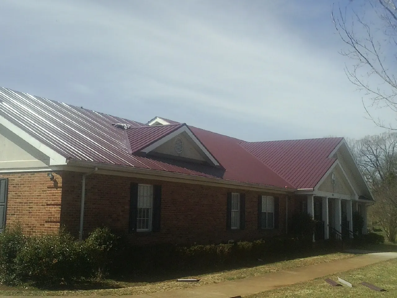 Red metal roof with gabled entries on a long brick building, from a Hail Damage Roof Repair job in Bethel Park