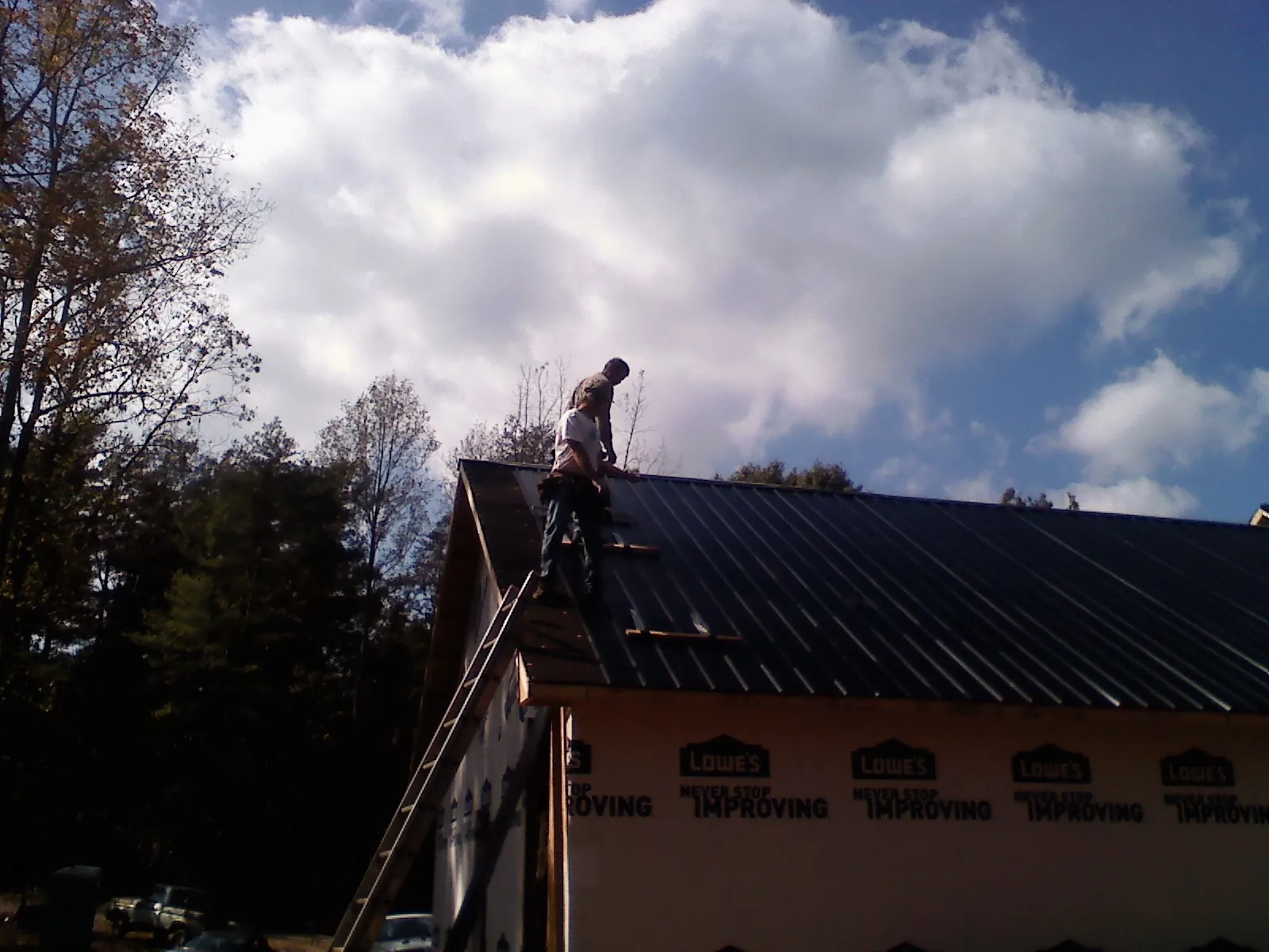 Roofer fastening dark metal panels high against a cloudy sky, from a Roof Inspection job in Bethel Park