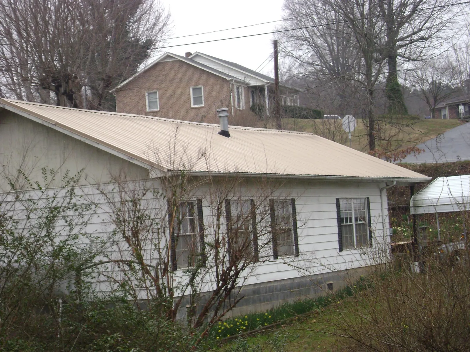 Tan metal roof on a white sided house set into a hillside — Commercial Roofing by Roofing Brothers in Bethel Park